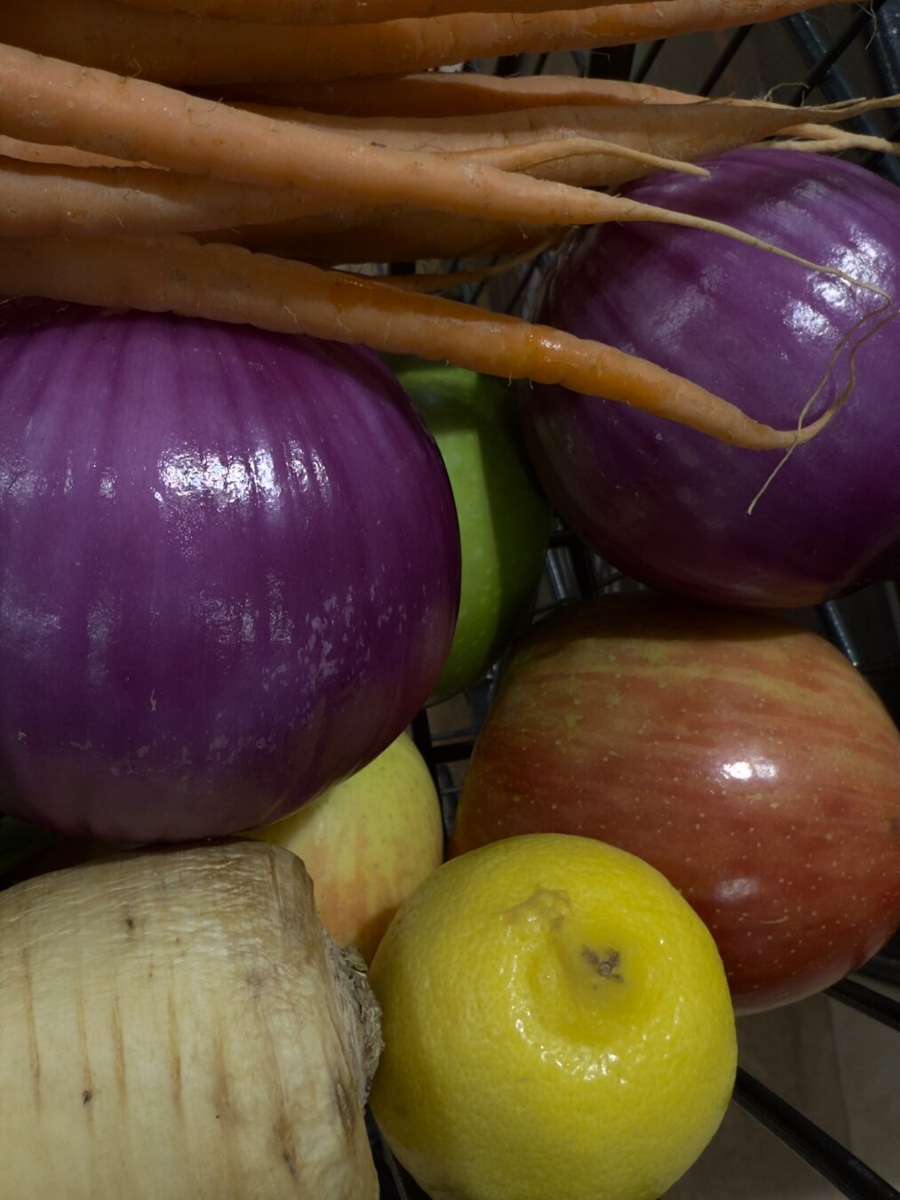 A close up shot of various colorful fruits and vegetables. Orange carrots, purple onions, red and green apples, a yellow lemon and a pale parsnip.