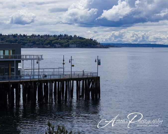 A picture of a large pier over looking a large body of water with hills and large sky in the background. This photo was taken in Seattle Washington USA