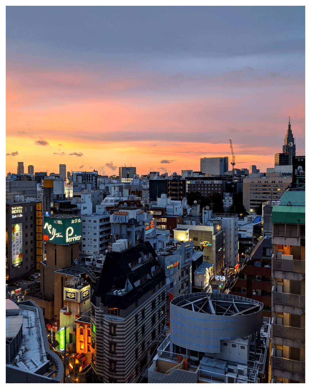 Picture of downtown Shinjuku City Japan taken in the evening hours from a high floor in a hotel. There's a colorful evening sky with clouds and numerous tall buildings with lights.