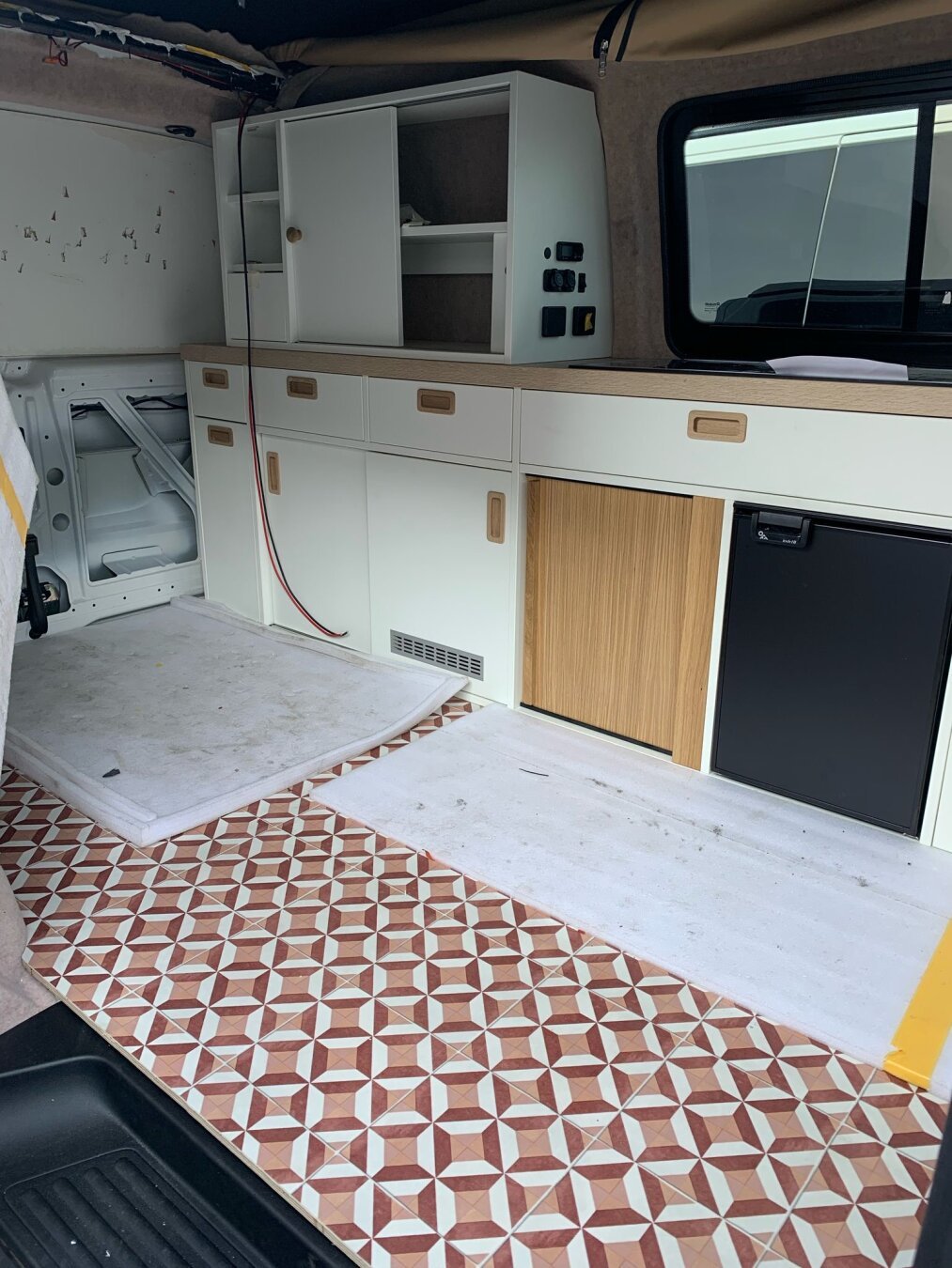 Work in progress interior of our camper van. The vinyl floor is in, as well as the kitchenblock. Wires hang from the roof andere there are protectional sheets on the floor.