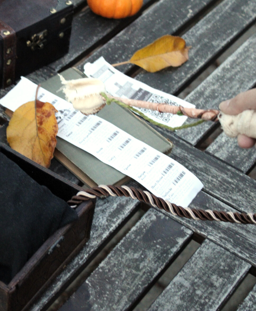 Wand above print-out of codes on a pleasant out-door table with boxes and leaves and a pumpkin arranged around.