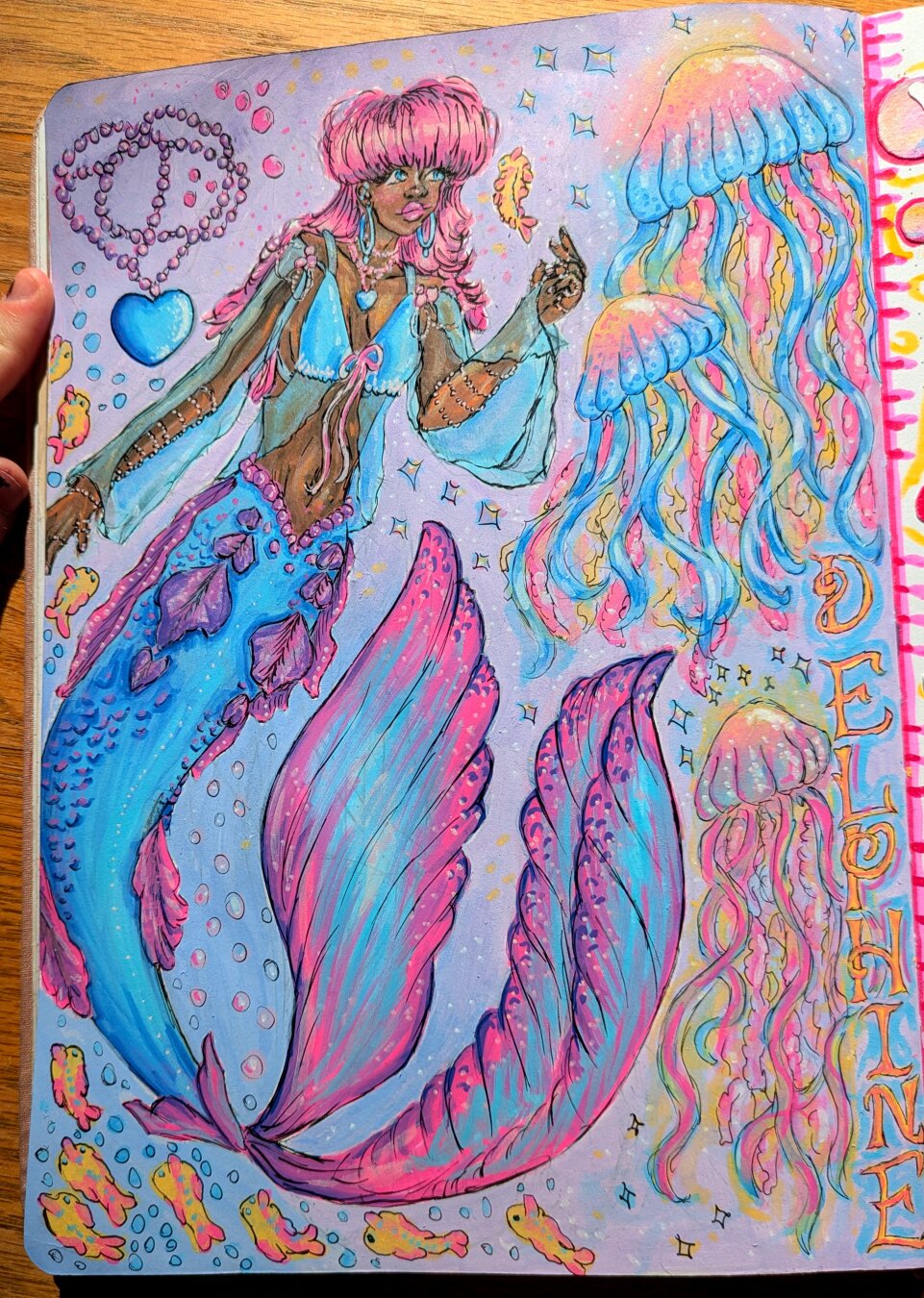 The finished drawing of my mermaid character Delphine! I love how she turned out with the jellyfish and the tail! Shes got pink hair, a blue top, a blue tail with pink ruffles, pink pearl jewelery, blue eyes, brown skin, and a blue heart pendant necklace