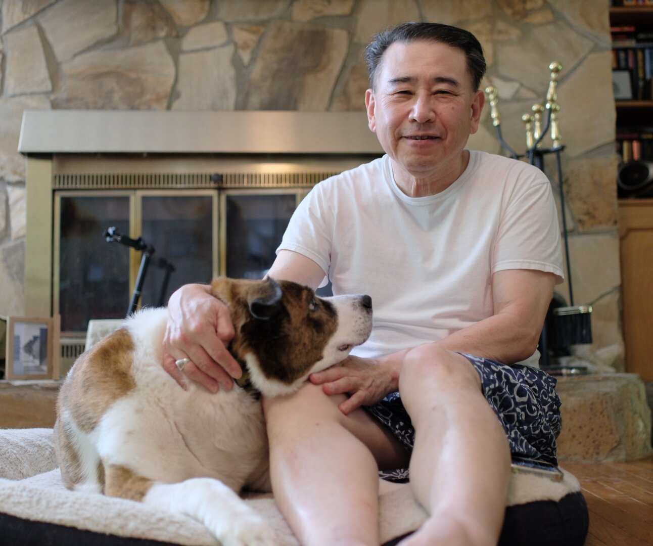 A man and his white and brown dog sitting on his bed as the dog rests (made him to) his chin on the man's thigh