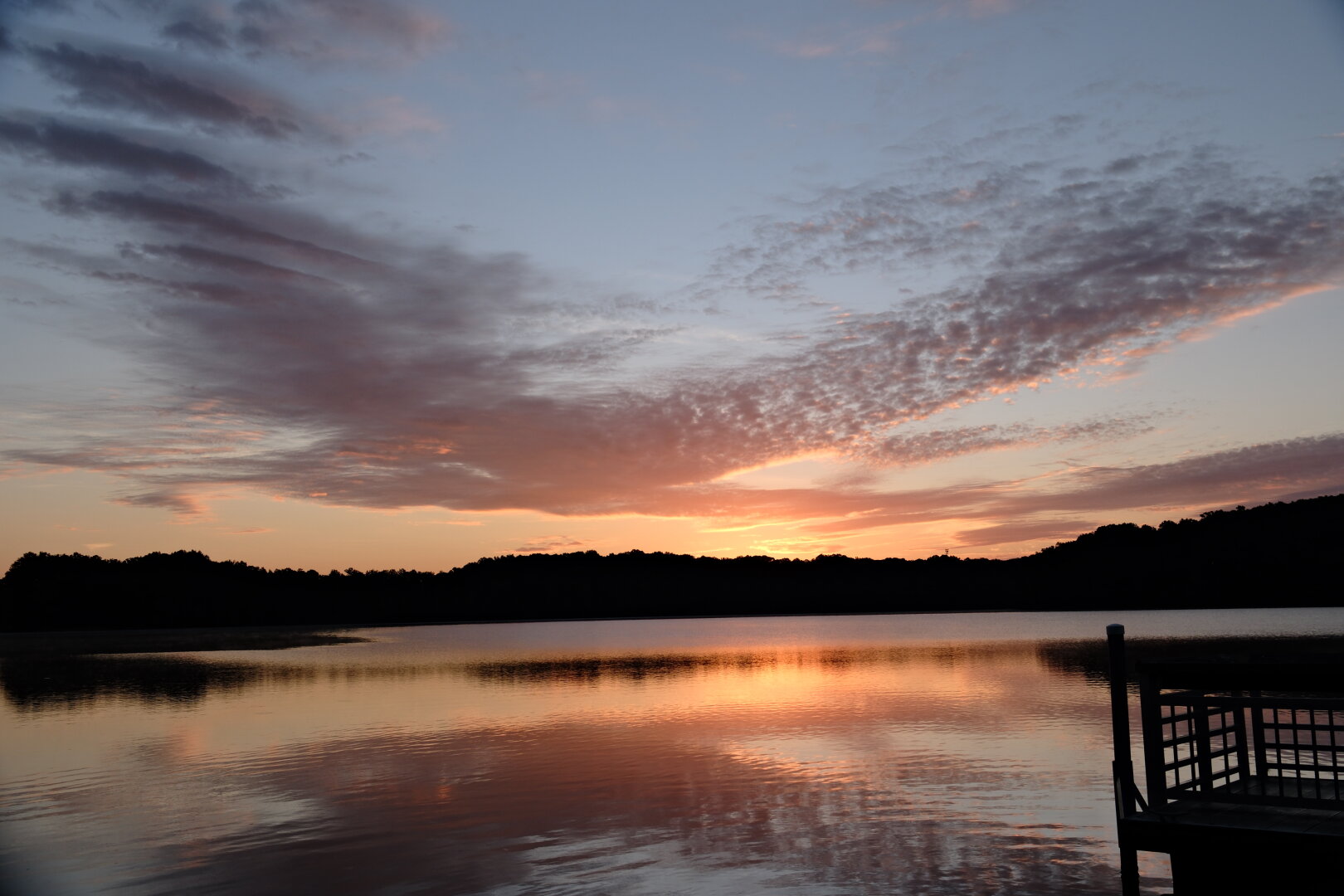 A lakeview with the rising sun paints the sky, clouds, and water orange.