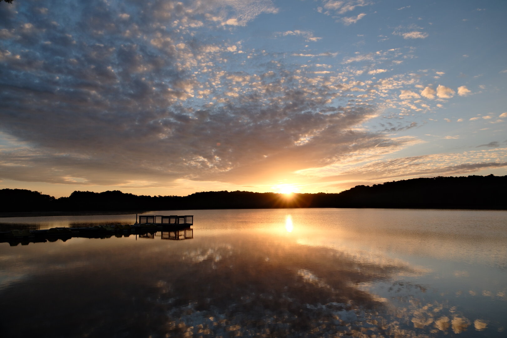 A lakeview with the rising sun paints the sky, clouds, and water orange.