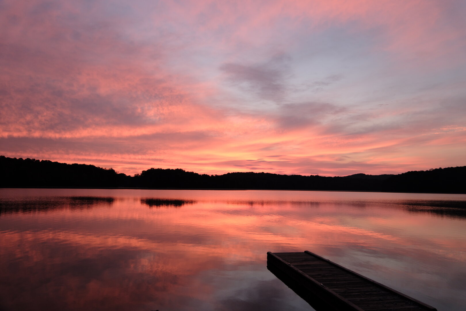 A lakeview at dawn as the sun paints the water, sky, and clouds red, orange, and pink.
