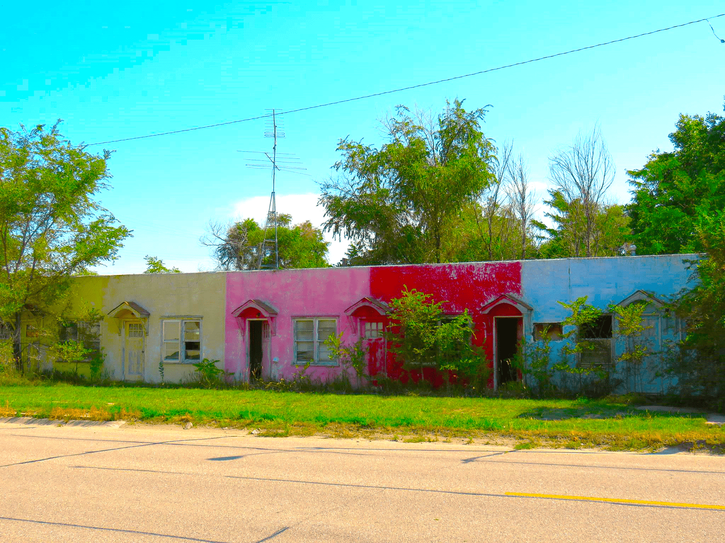 Abandoned motel in the process of becoming overgrown with trees and plants, but still very visible with a multicolored facade.