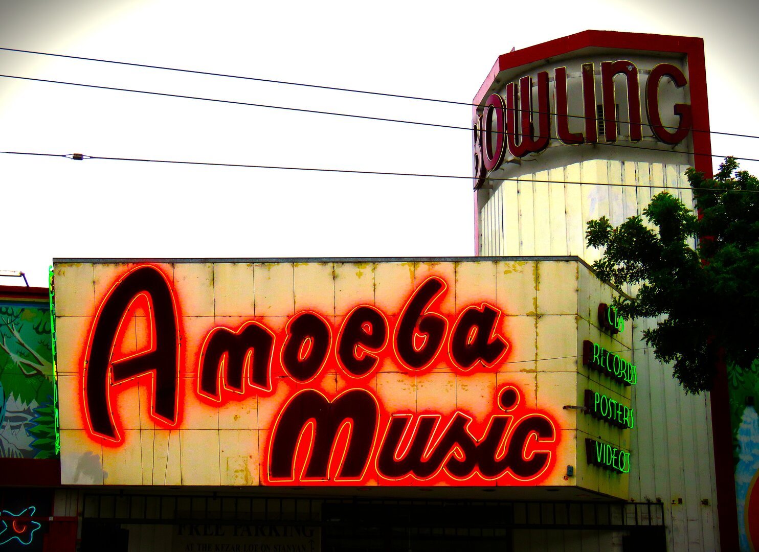 A cracked and worn off-white overhang with a red neon sign on a black background reading Amoeba Music. A slightly taller structure on the right has a red sign reading Bowling at the top. The music store is located in what used to be a bowling alley.