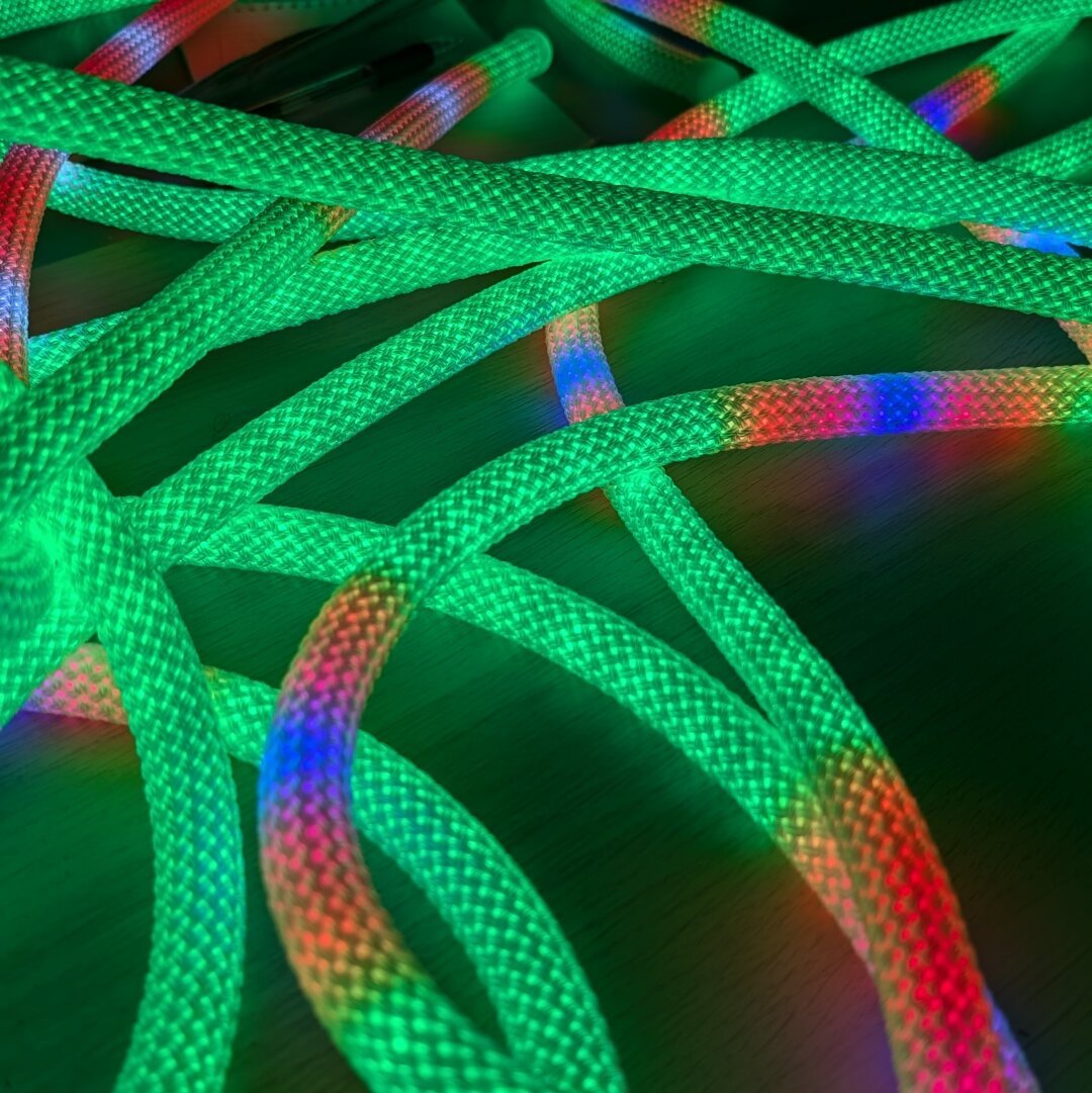 Many strands of glowing, braided LED rope weaving around each other, lit up mostly green and with some red patches.