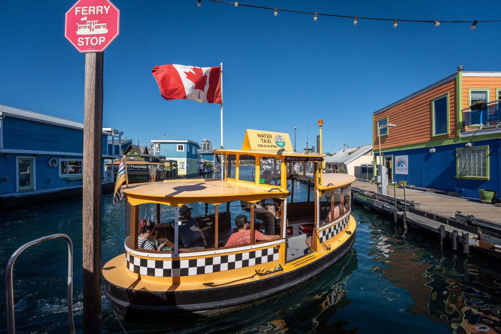 A small boat decorated in classic taxi yellow and checked paint flies a Canadian flag as the boat delivers passengers to the ferry stop - indicated by an octagonal red sign mounted atop a post.