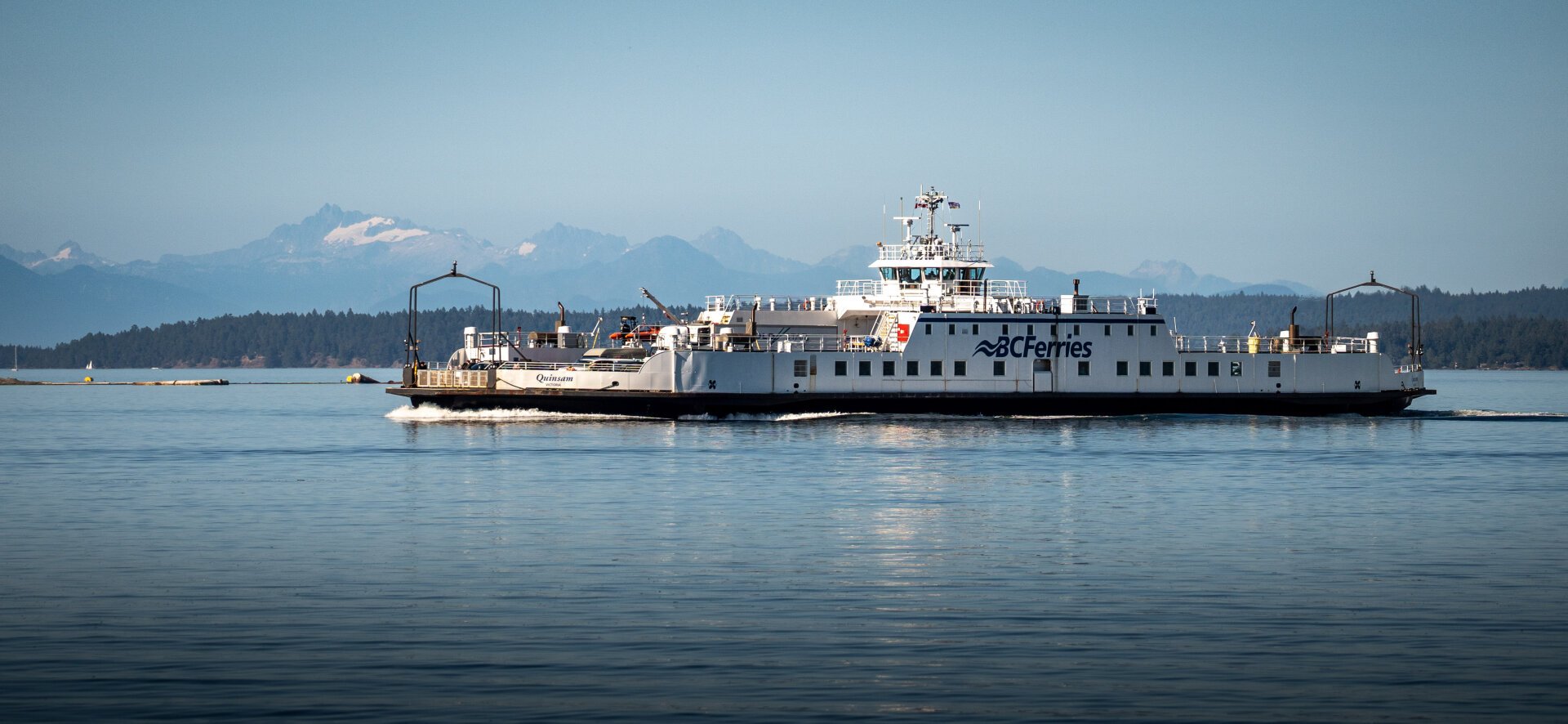 A white ferry with a blue "BC Ferries" logo on the ocean, with a background of trees and mountains typical of the Gulf Islands in the Salish Sea off the west coast of British Columbia.