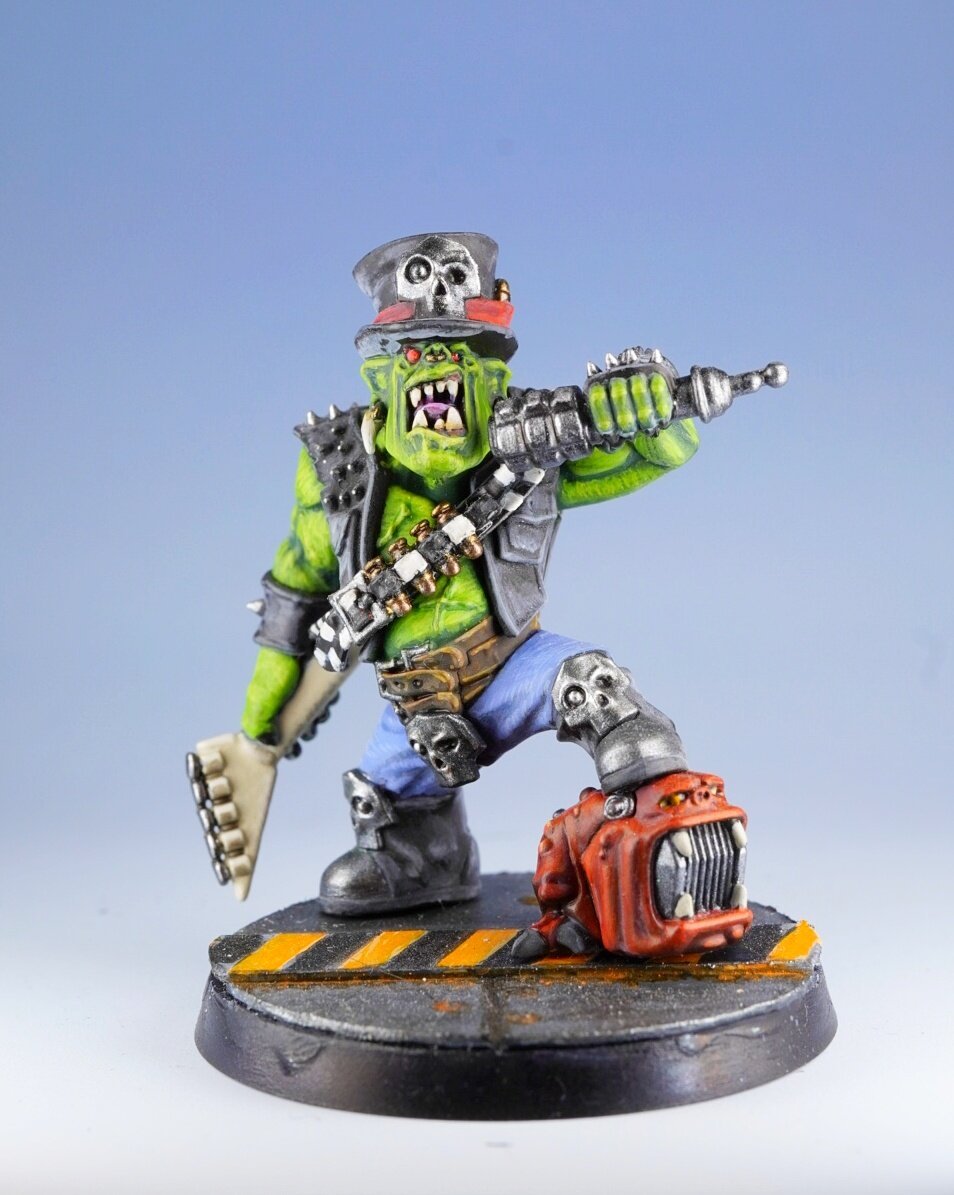 Warhammer Commemorative Series Goff Rocker miniature.

Its a big ork with an electric guitar, a hat and a squig amplifier. View from the front.