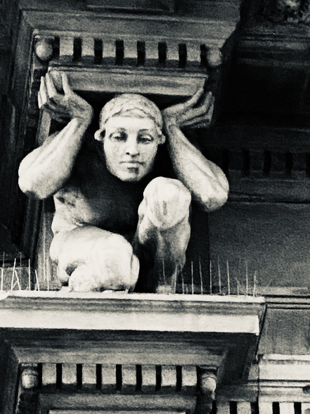 Picture of a stone figure carrying the upper part of a pillar, while kneeing.