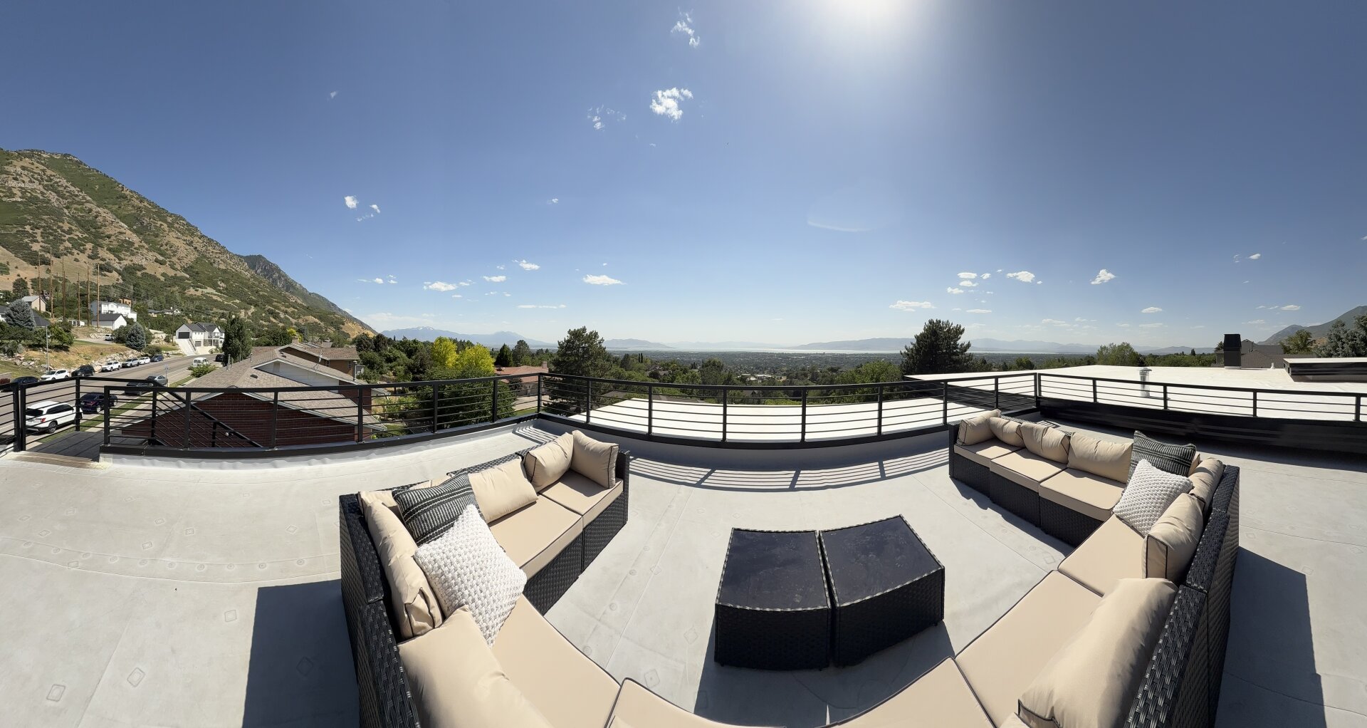A panoramic shot of a rooftop patio overlooking a mountain range and a large body of water in the distance.