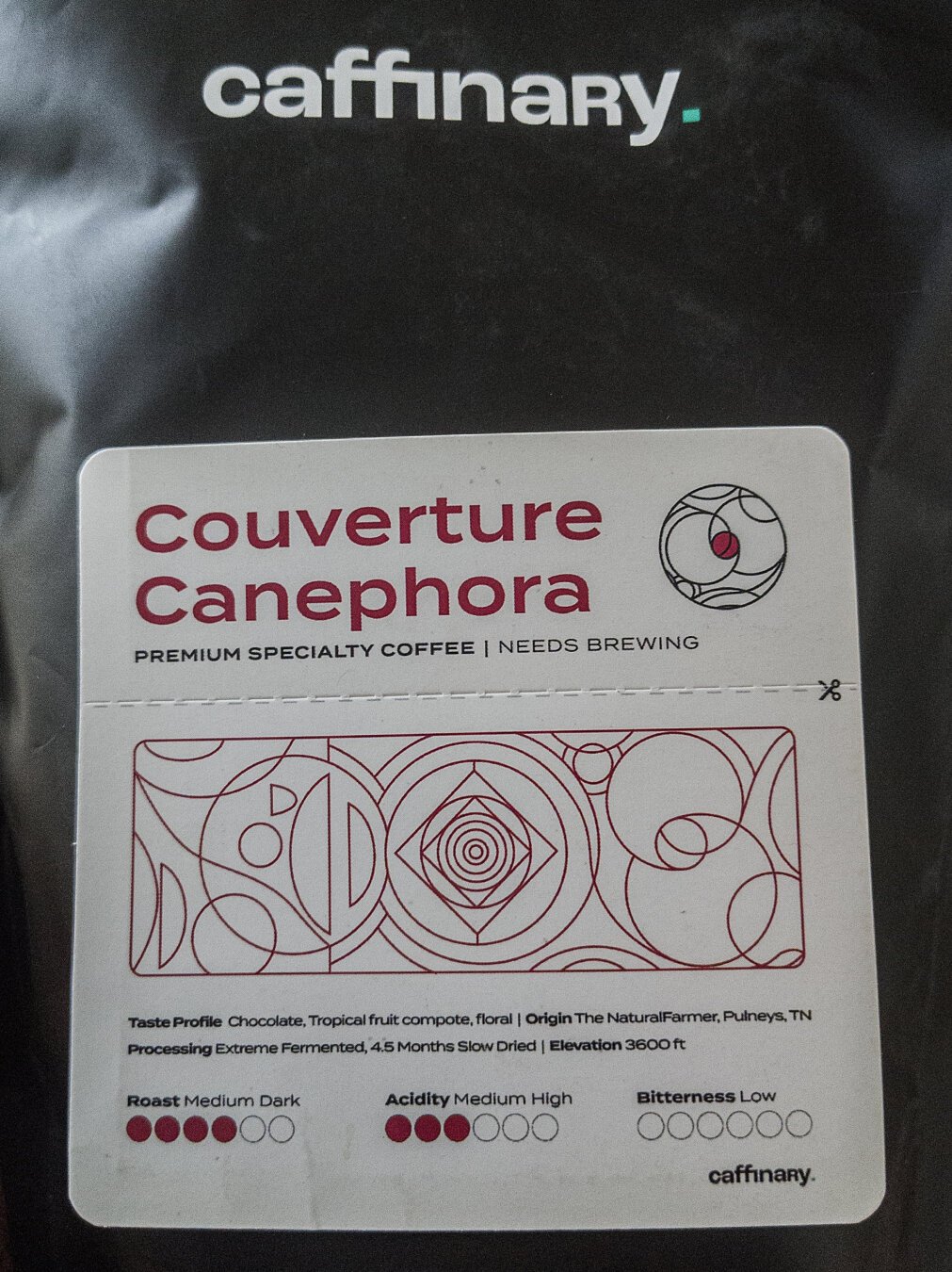 a black plastic coffee bag with a white label and red, black iconography and text. there is a 