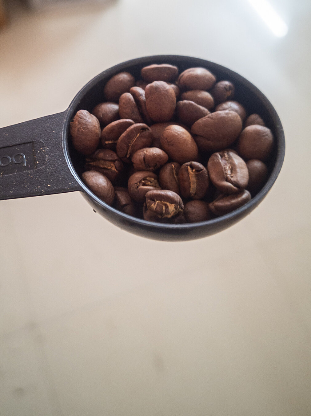A black semi spherical scoop containing brown coffee beans.
