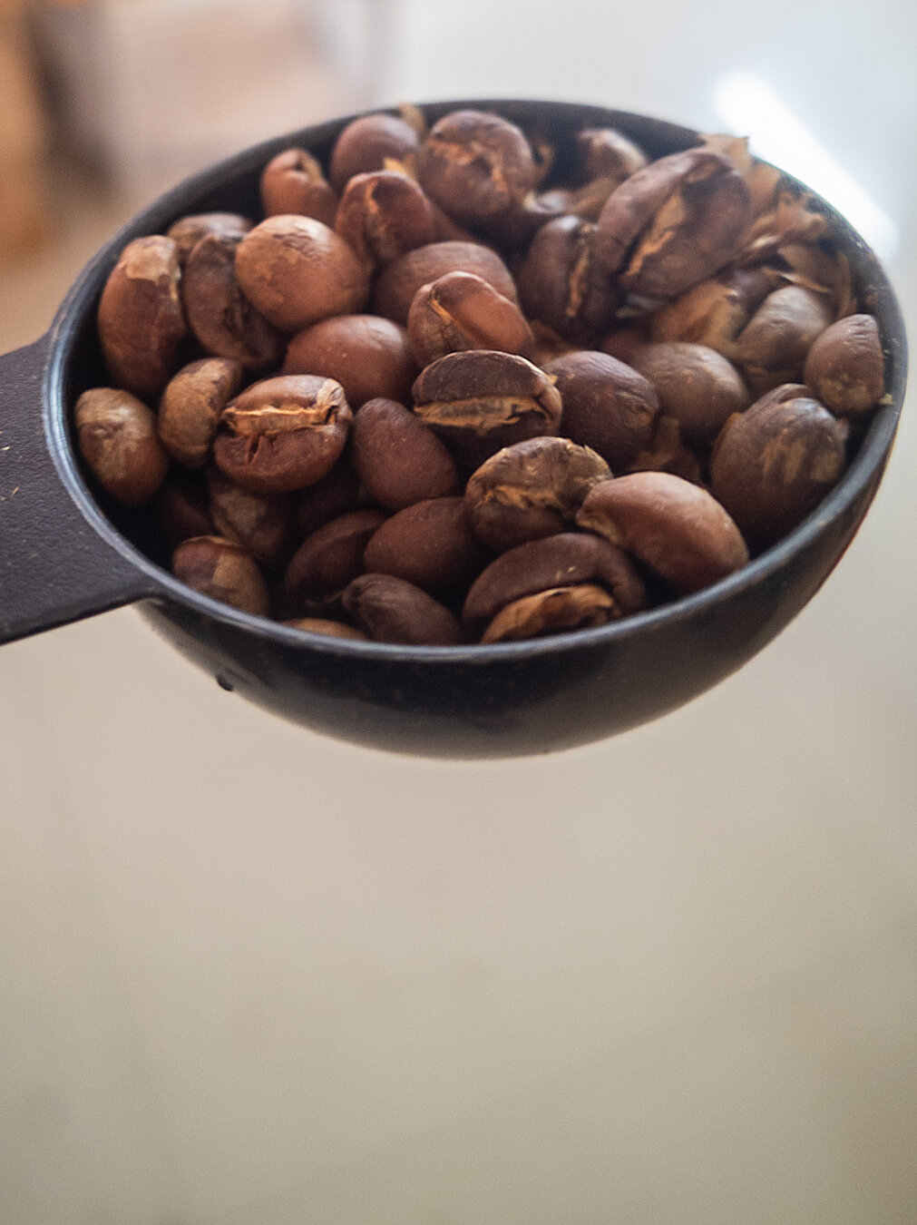 A black semi spherical scoop containing brown coffee beans.
