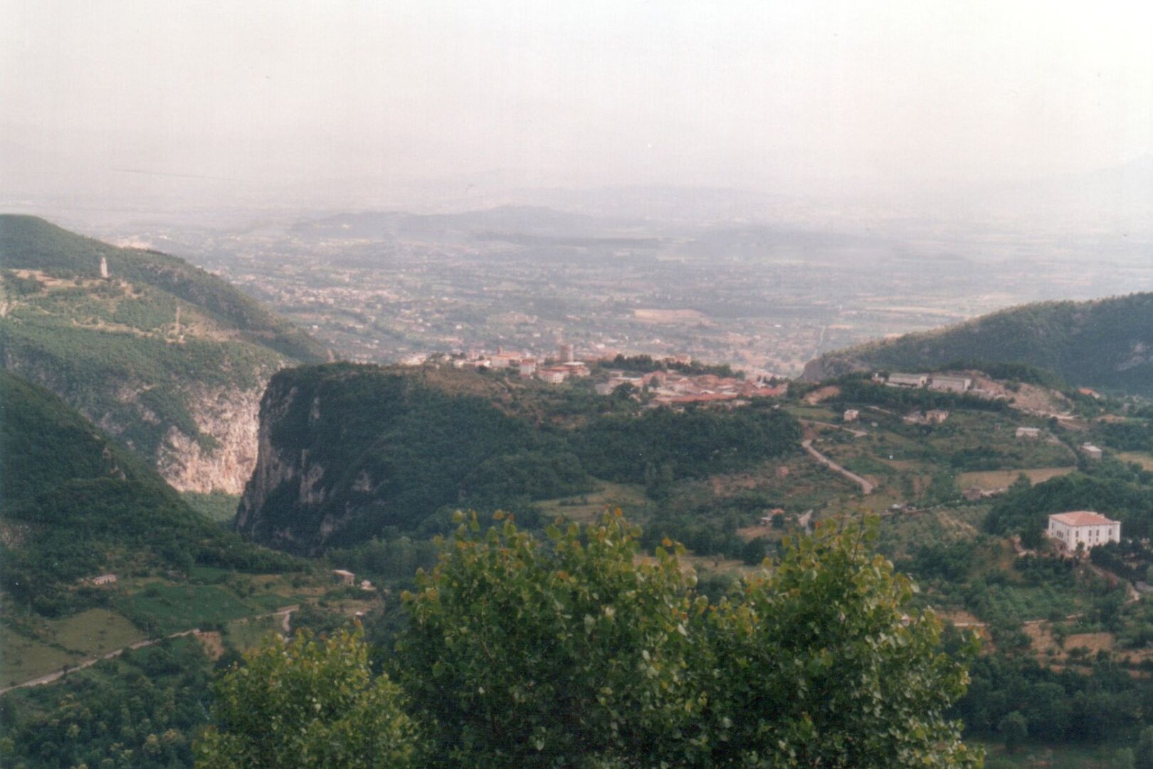 Vista dall'alto di un borgo di montagna, con un castello visibile al centro, edificato su un rilievo pianeggiante posto tra più alti monti boscosi