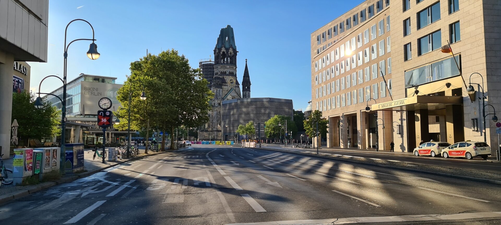 Menschen- und autoleere Straße führt auf die Gedächstniskirche in Berlin zu. Die flachstehende Sinne beleuchtet die Szenerie.