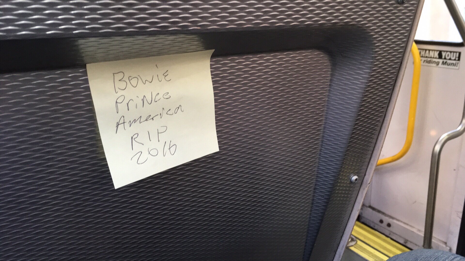 sticky note on a Muni train saying: BOWIE / PRINCE / AMERICA / RIP / 2016