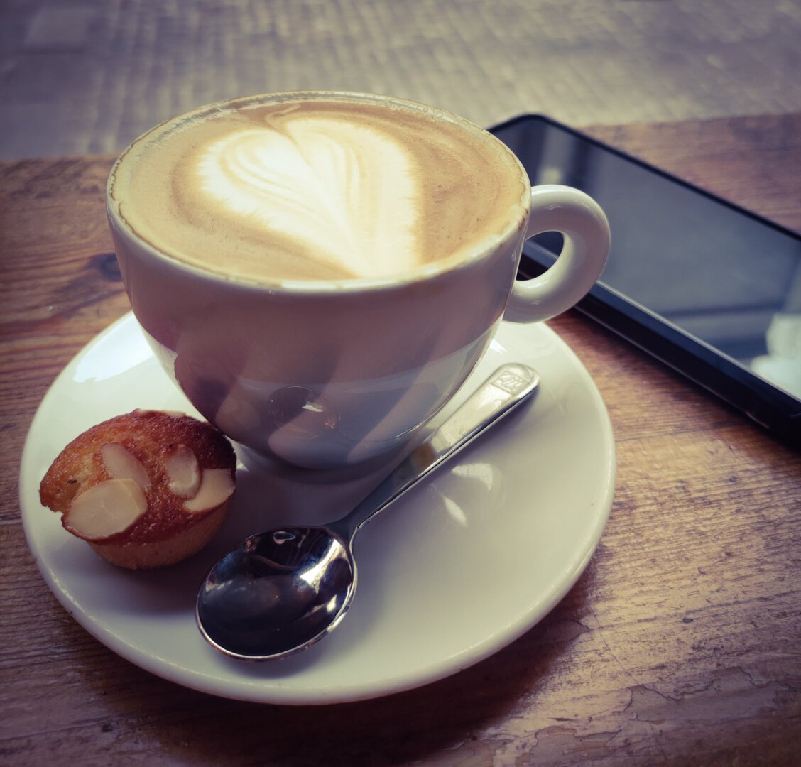 Fotografía de una taza de café y un teléfono móvil en segundo plano.