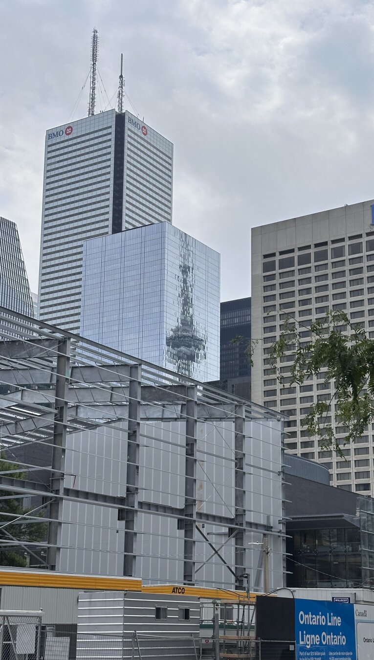 Large office towers along with a hotel in the background. In the tower that is in the centre of the image, there is the reflection of the iconic CN Tower in the building’s all-glass cladding.