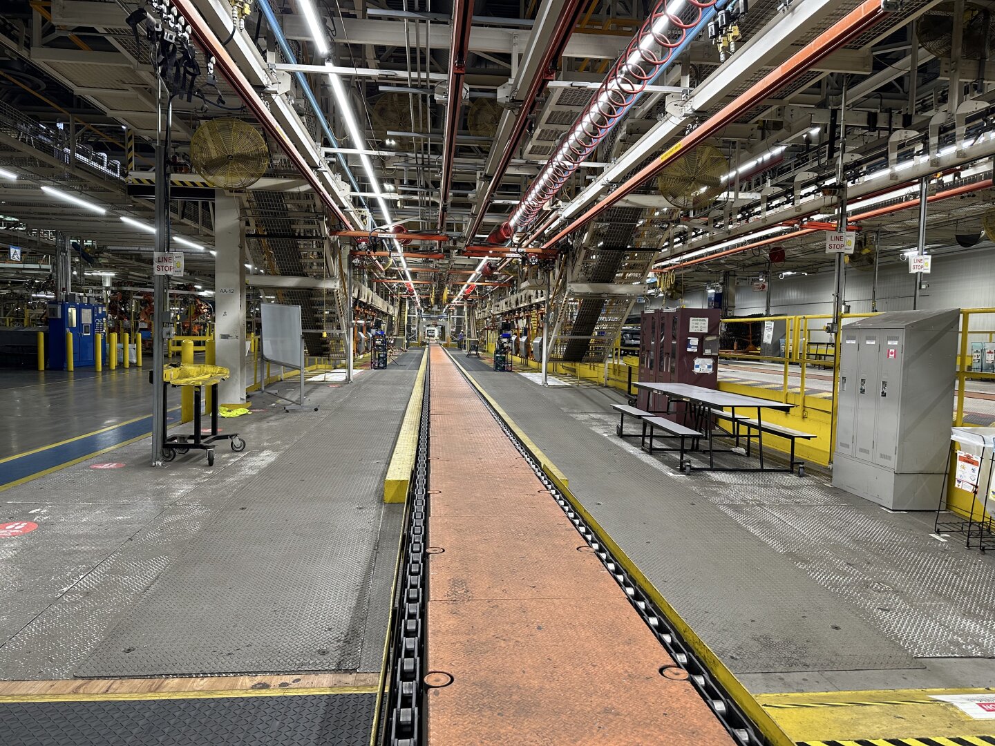 Looking from one end of a now empty automotive assembly line. The conveyor line that now has no cars on it, along with the overhead lights and equipment, all seem to converge far into the distance.
