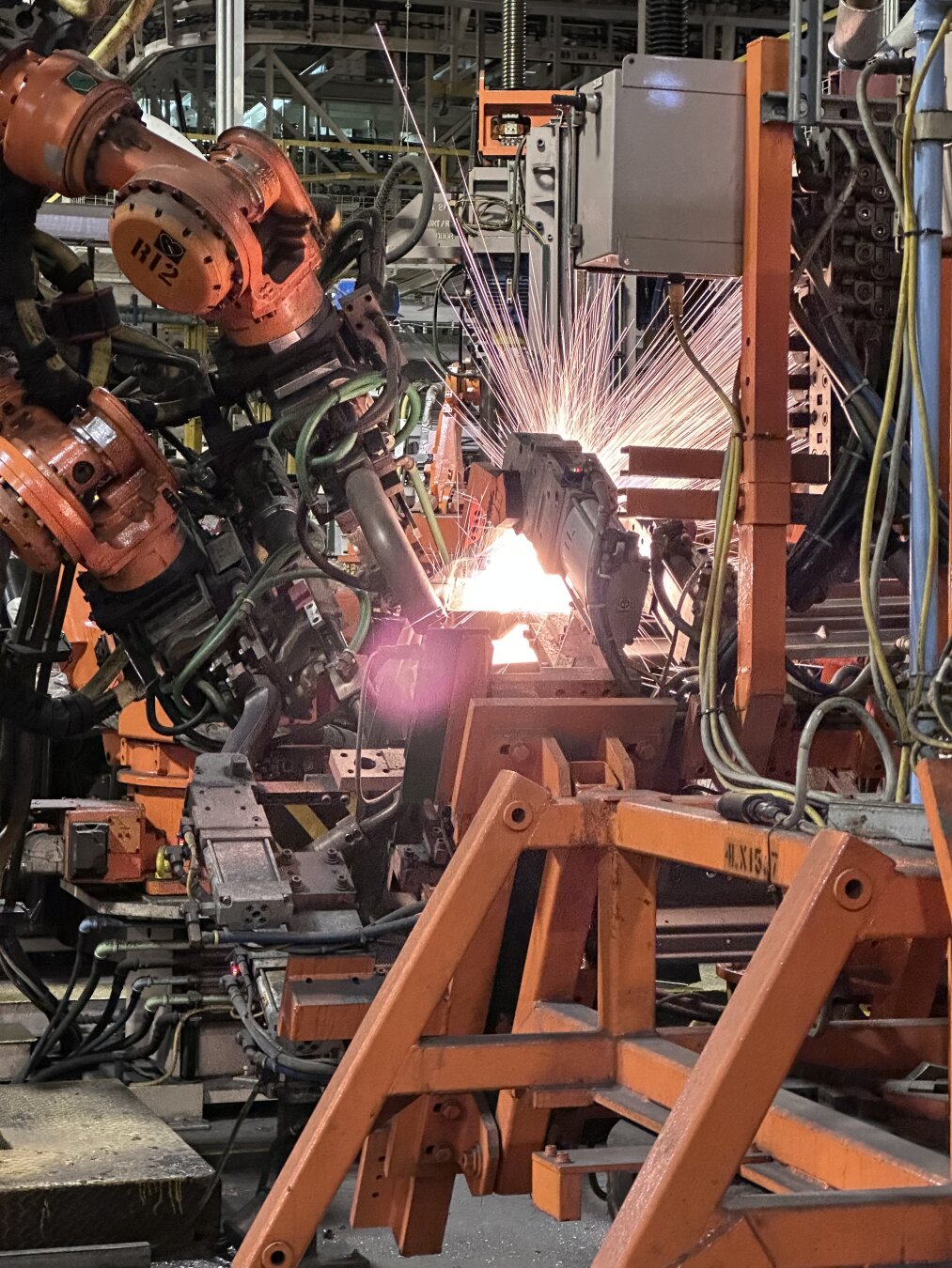 A robotic weld cell in an auto assembly plant. The robots are completing a “pinch weld” which has caused the molten metal to spray out in a fantastic show of light, similar to fireworks going off.