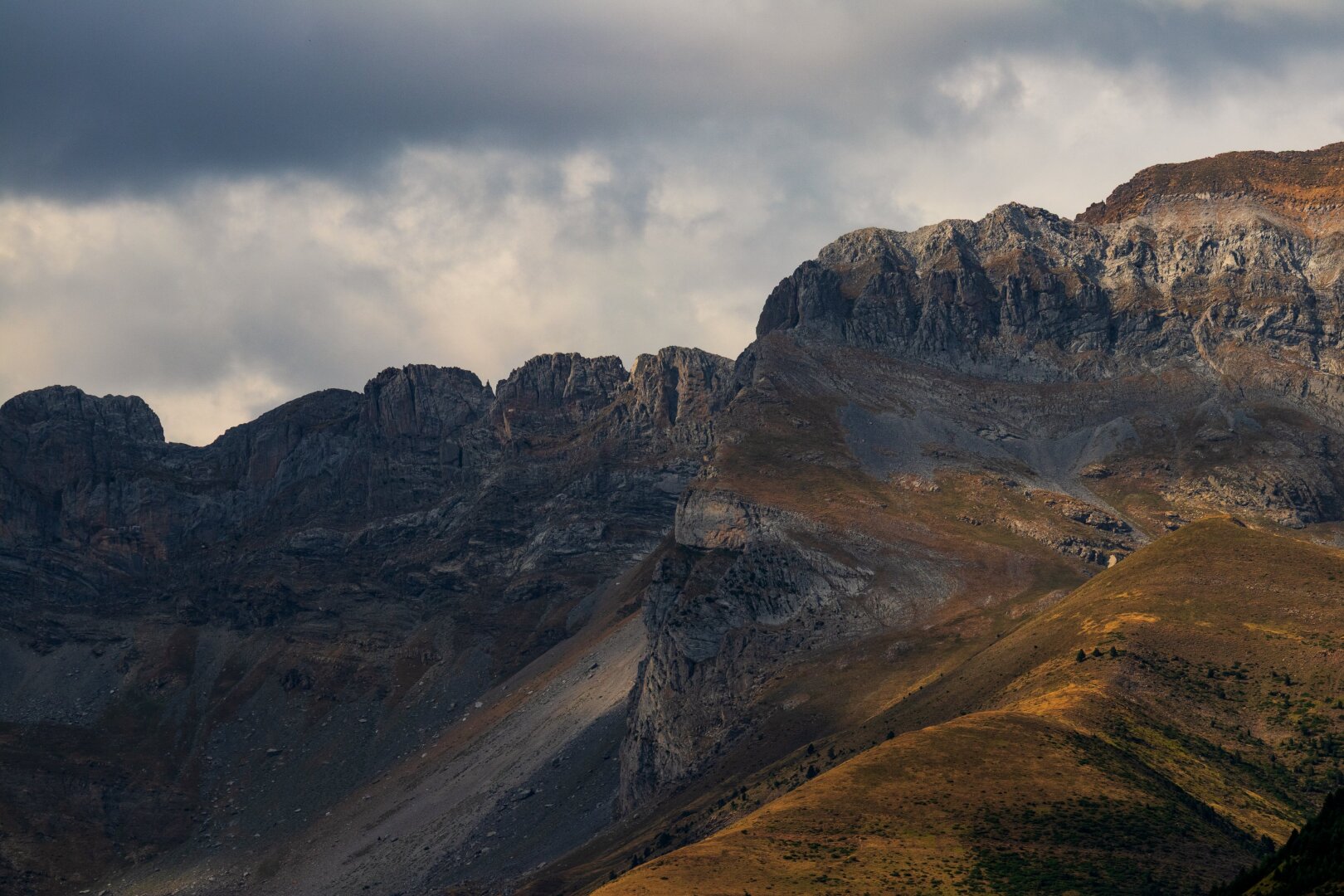 Español: una toma de primer plano de montañas escarpadas y rocosas bajo un cielo nublado y dramático. Las laderas inferiores son de color marrón dorado.

English: aclose-up shot of rugged, rocky mountains under a dramatic cloudy sky. The lower slopes are a warm golden-brown.