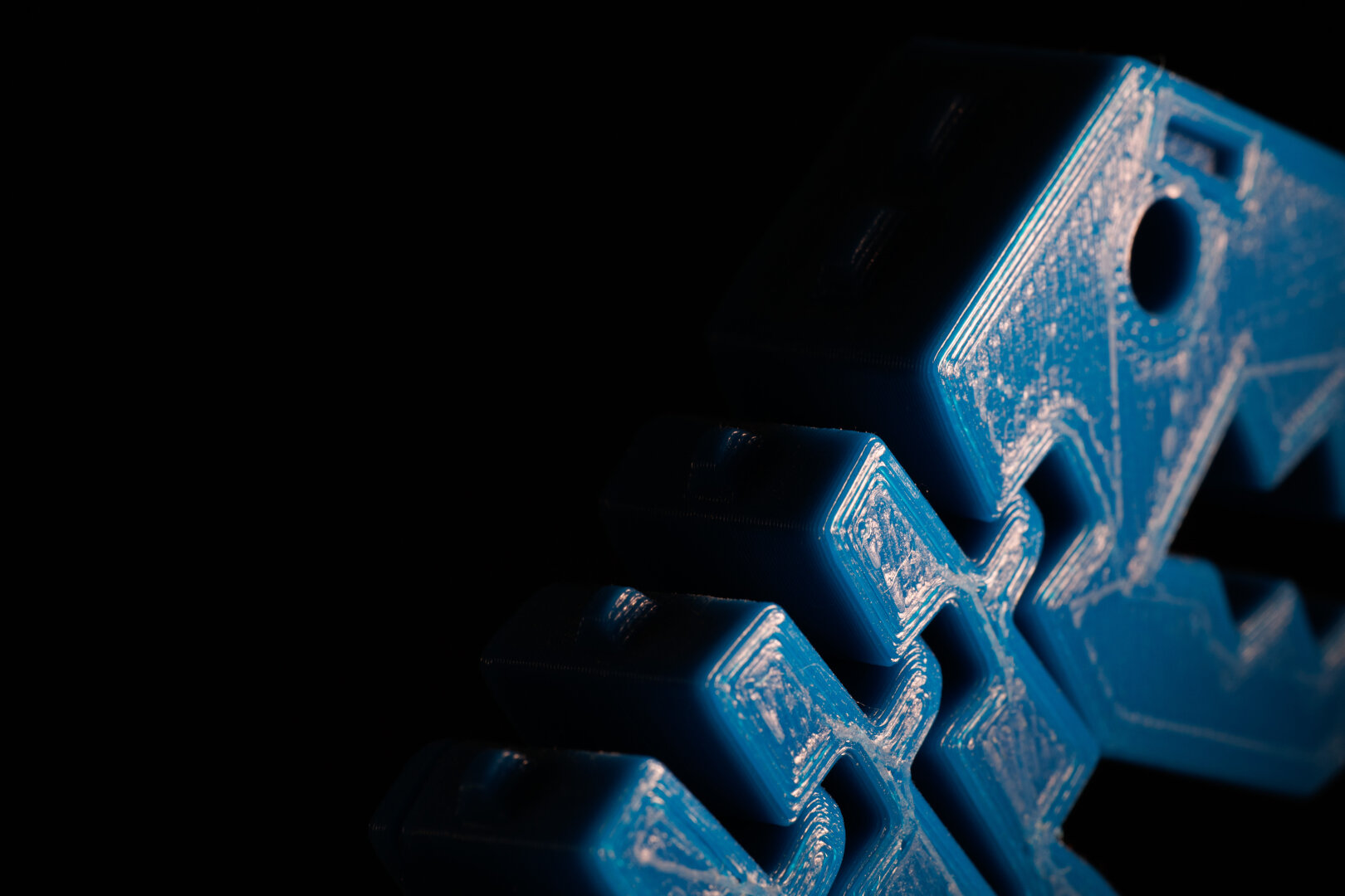 A close up of a blue, 3d-printed dinosaur. Harsh light from the left, black on the right, showing the shape of the model.