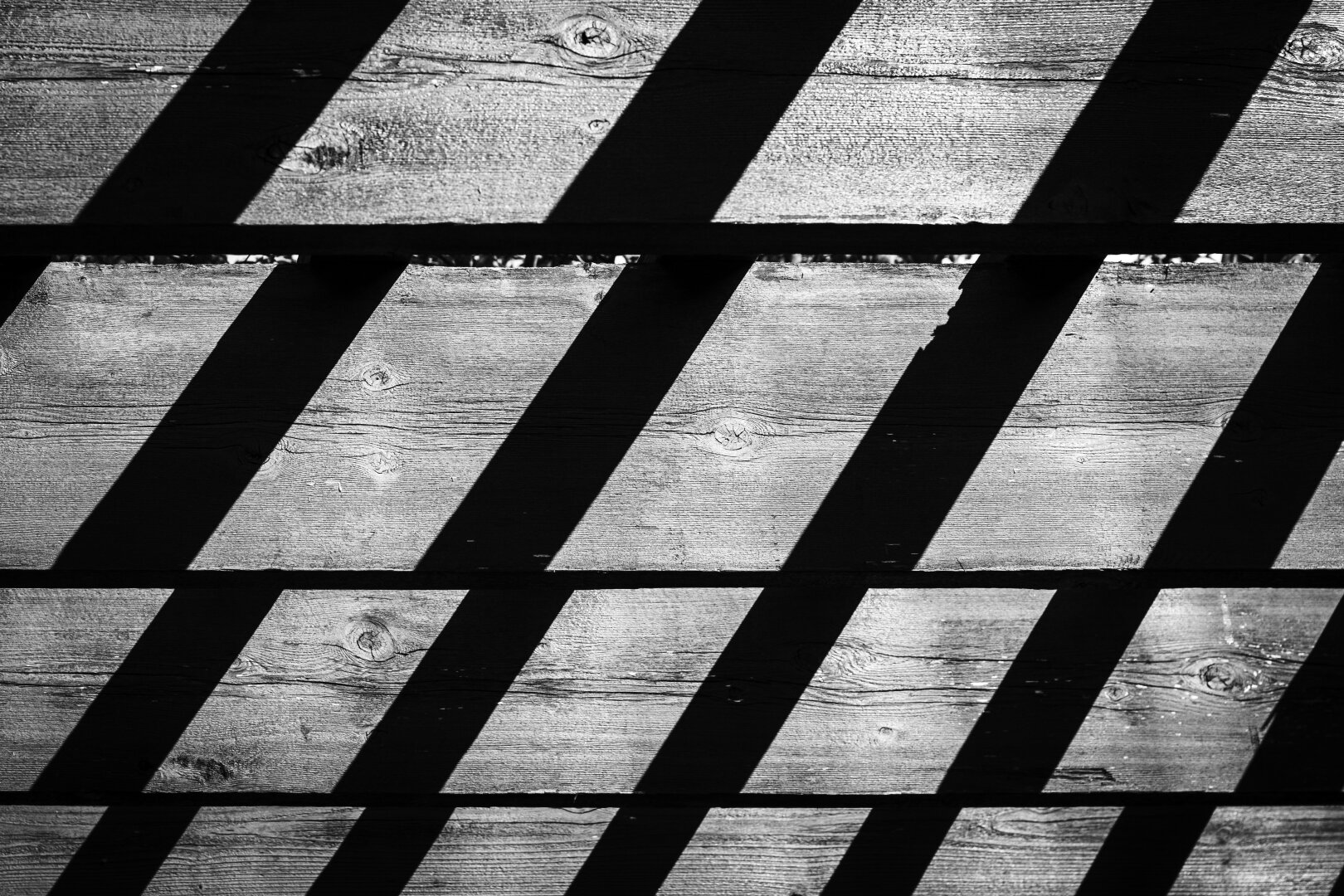 Shadows on the wooden slats of the roof of a pergola, in black and white.