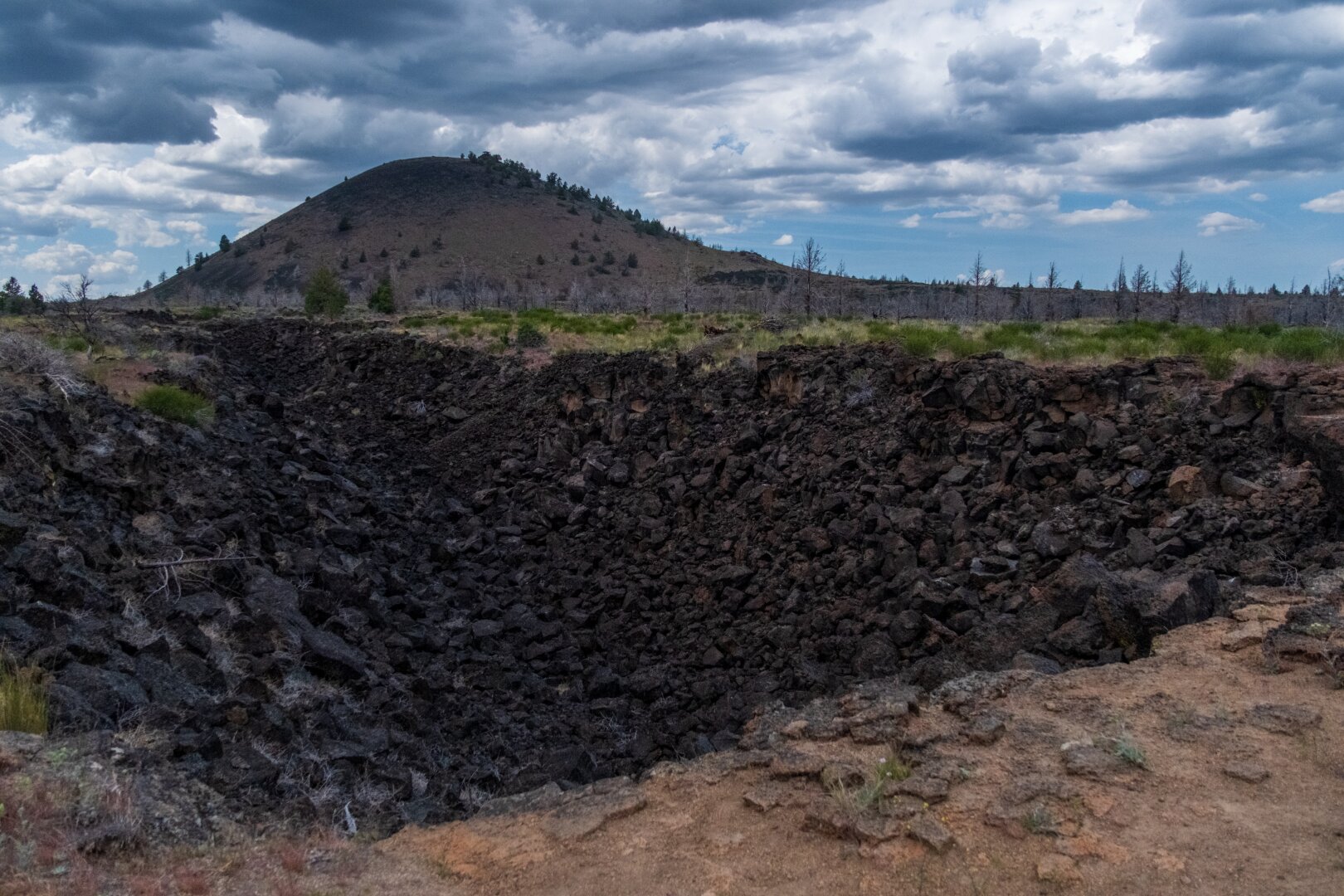 A rocky hole in the ground in the foreground, and a cone-shaped hill in the background. [Fuji X-T5 / Tamron 18-300]