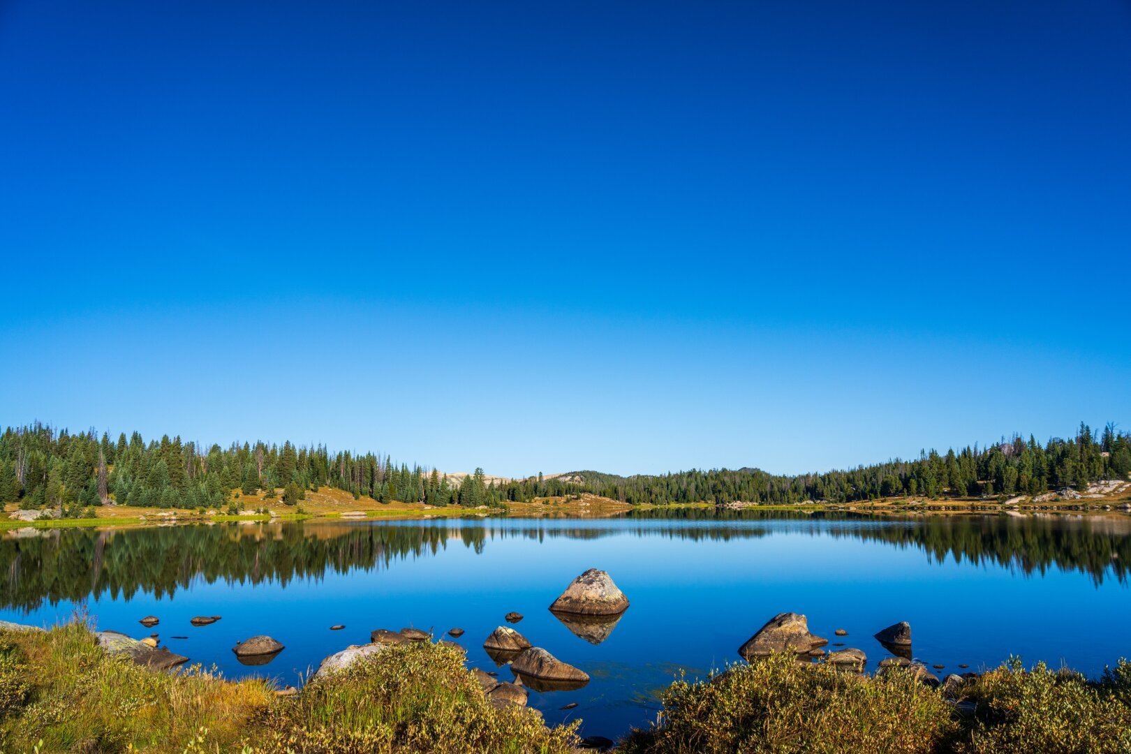 A lake with rocks in it stretches away in a shallow valley. [Sony A7R V / Tamron 25-200]