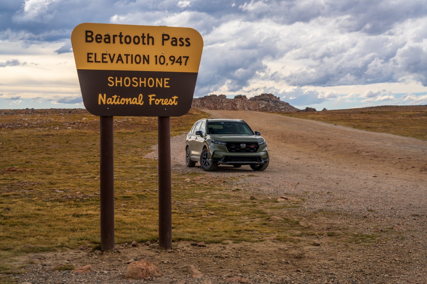 A sign indicates the top of the Beartooth Pass, at 10,947 feet, with a car in a dirt lot behind. [Sony A7R V / Tamron 25-200]