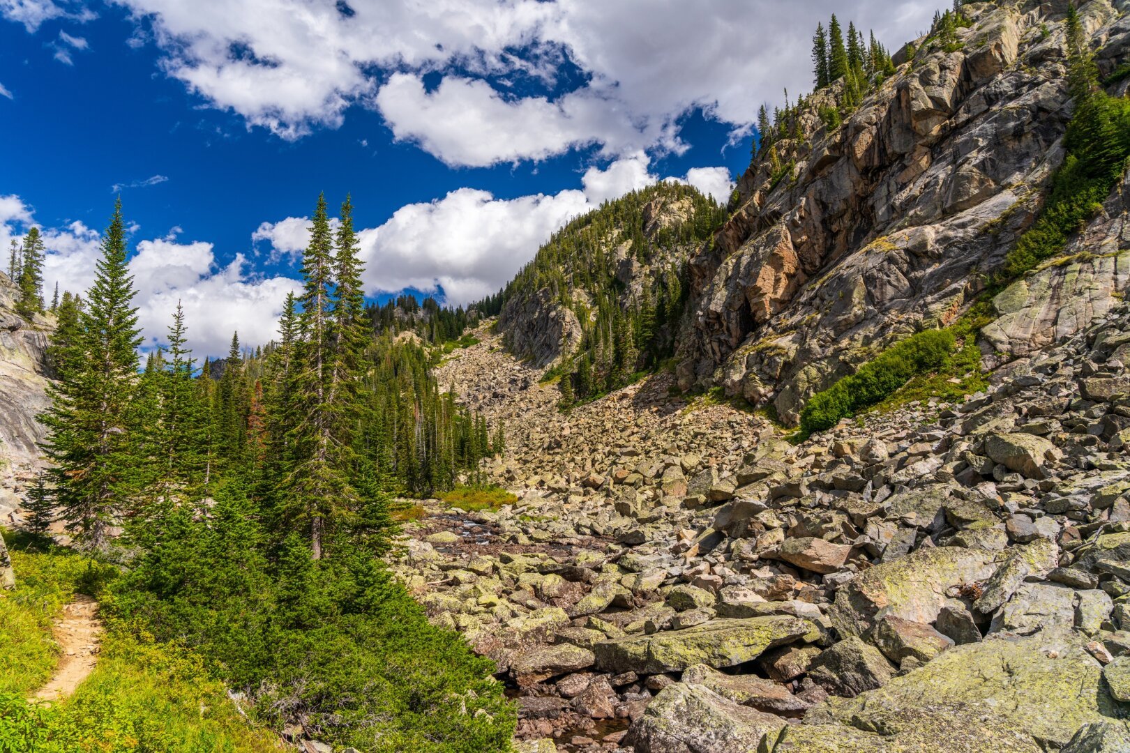 A creek runs through a very rocky area, with a trail to the left. [Sony A7R V / Tamron 25-200]