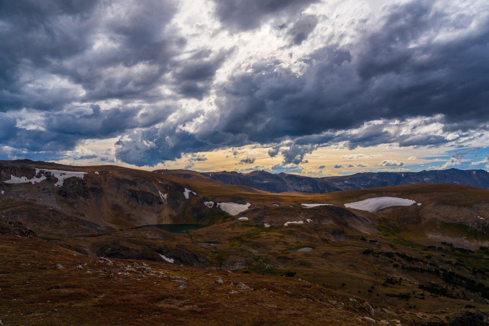 A rolling landscape of low orange grasses, below a cloudy sky, with a bit of snow. [Sony A7R V / Tamron 25-200]