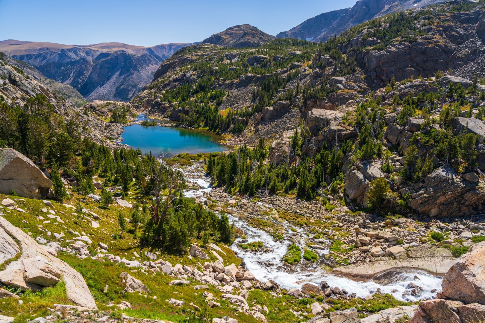 Water runs down a mountainside toward a small lake, under blue skies. [Sony A7R V / Tamron 25-200]