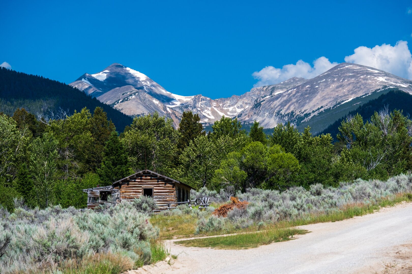 An abandoned log house in front of tall mountains. [Fuji X-T5 / Tamron 18-300]