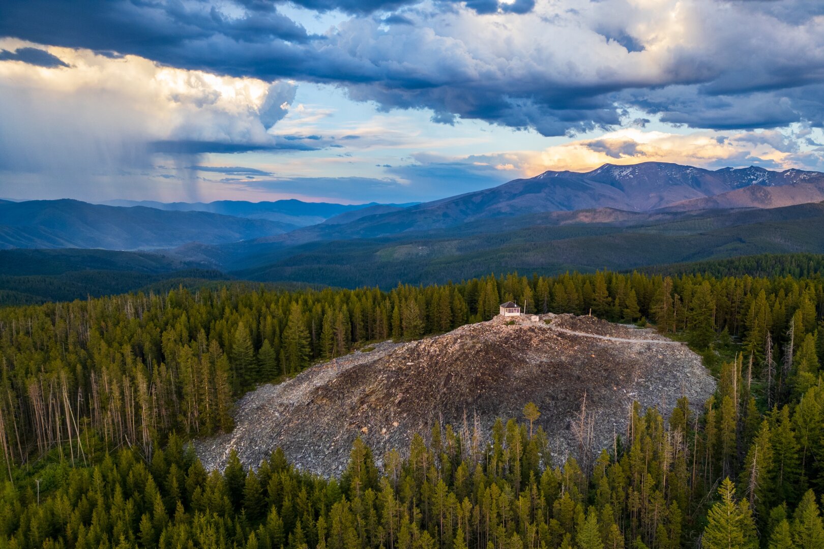 A fire lookout sits on a rocky hill amidst trees, with dramatic skies behind. [DJI Mini 3 Pro]