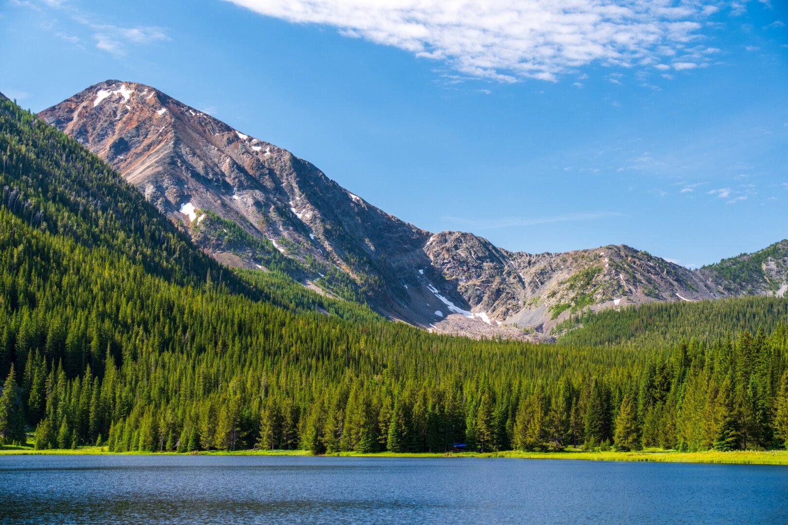 A large mountain looms behind the forest on the edge of a lake. [Fuji X-T5 / Tamron 18-300]
