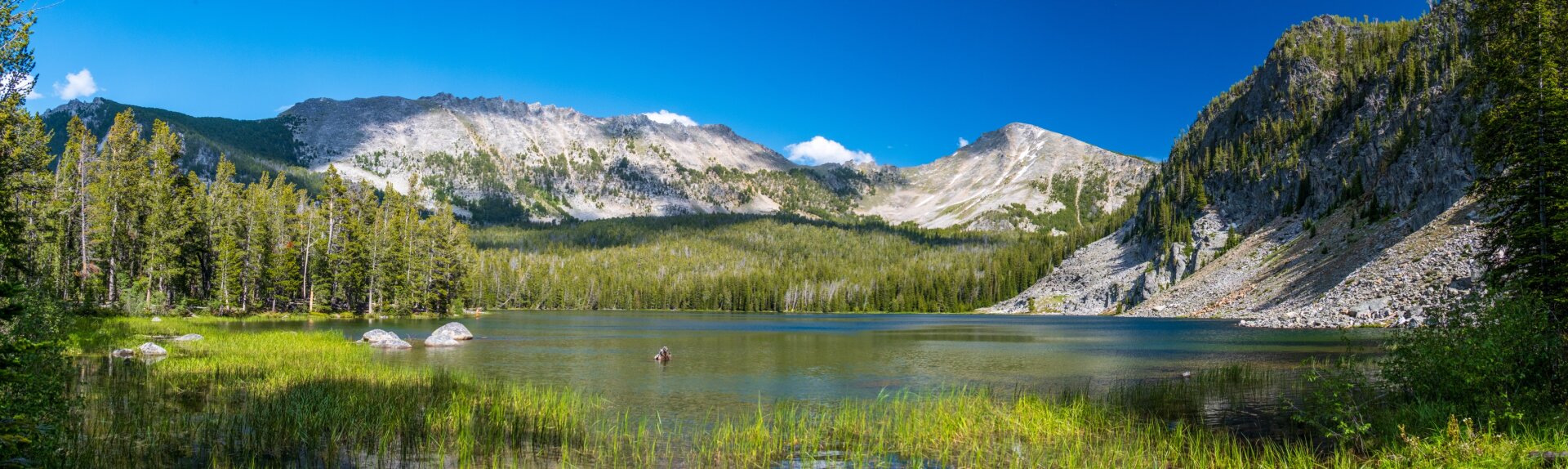 A panorama showing a large lake with a talus slope on one side, trees on the other, and mountains behind. [Fuji X-T5 / Tamron 18-300]