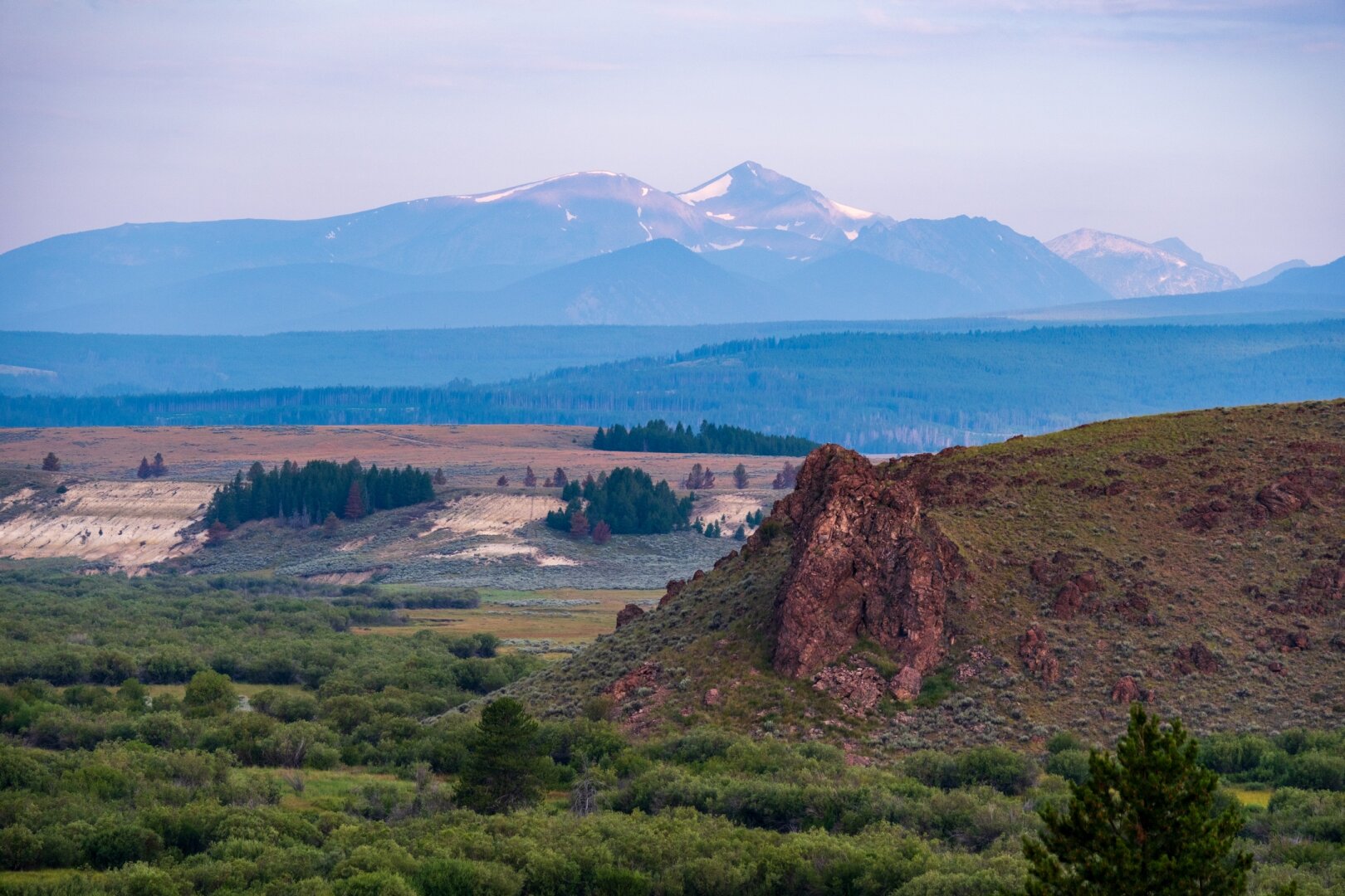 A mountain range rises in the distance behind greenery and a rocky outcrop. [Fuji X-T5 / Tamron 18-300]