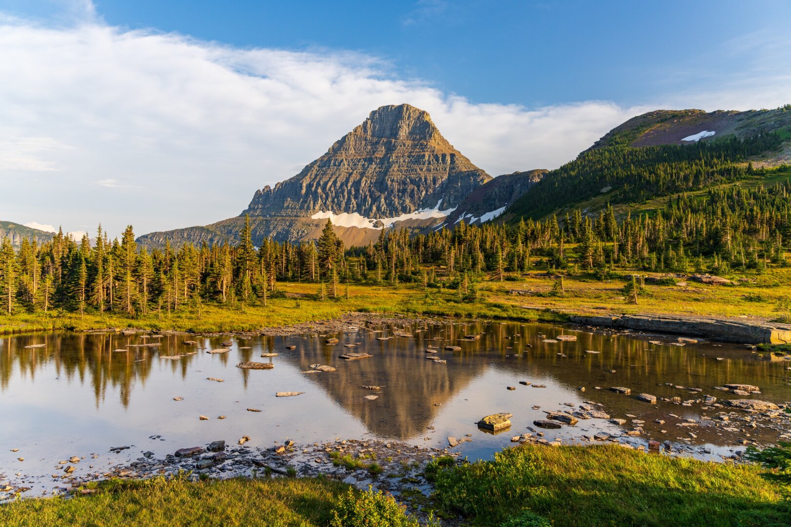 A mountain lit by evening light is reflected in a lake with rocks in it. [Sony A7R V / Tamron 25-200]