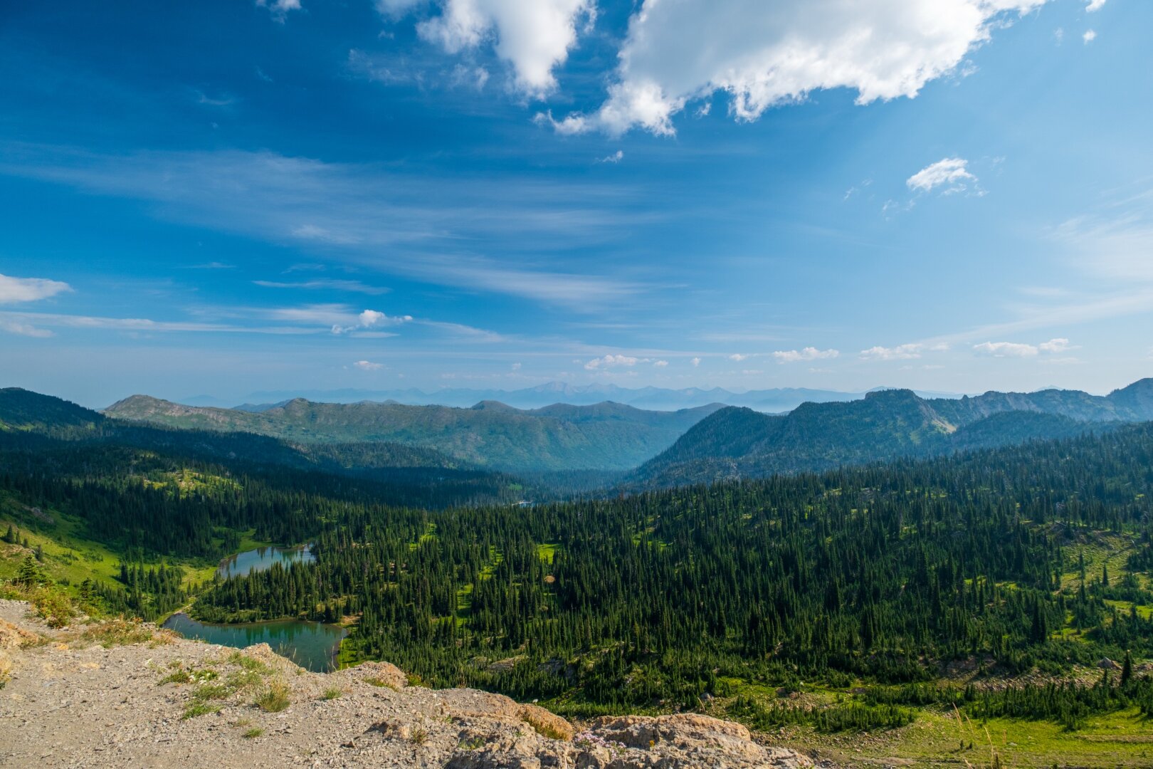 Under a wide blue sky, two lakes sit amidst trees in front of mountains in the distance. [Fuji X-T5 / Fuji 10-24 WR]