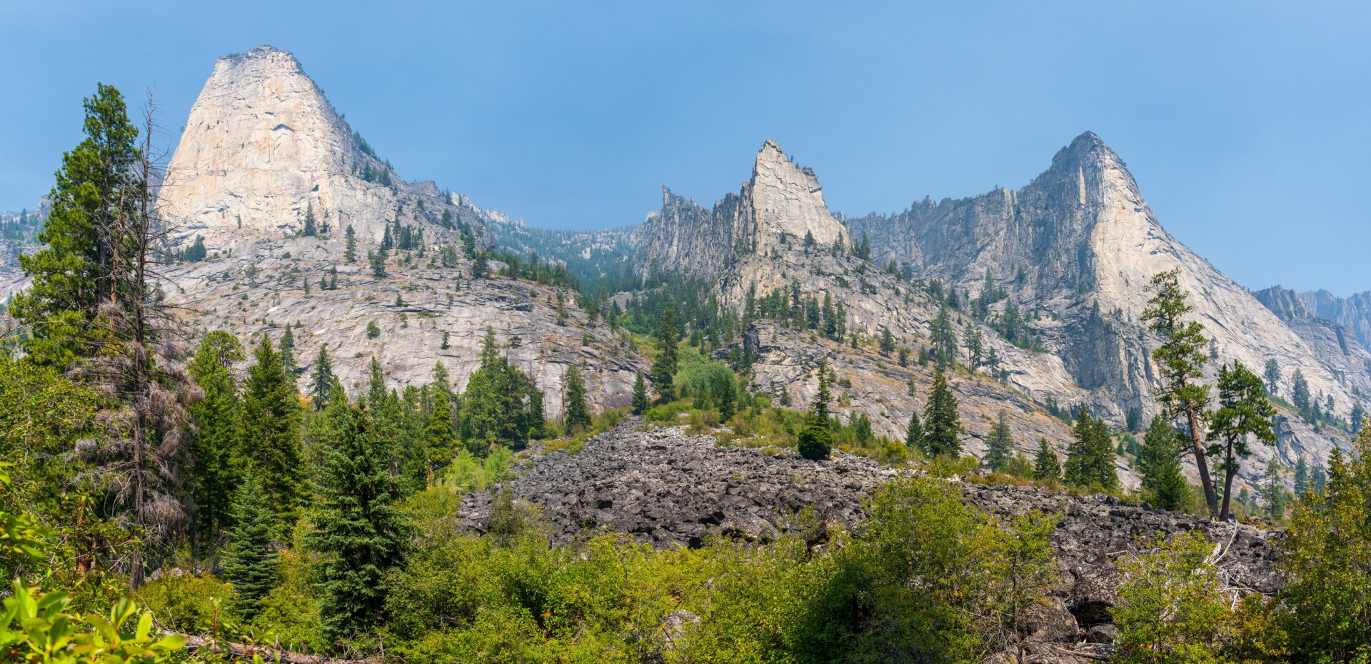 Three mountain spires rise above greenery into a kinda-smoky sky. [Sony A7R V / Tamron 25-200]