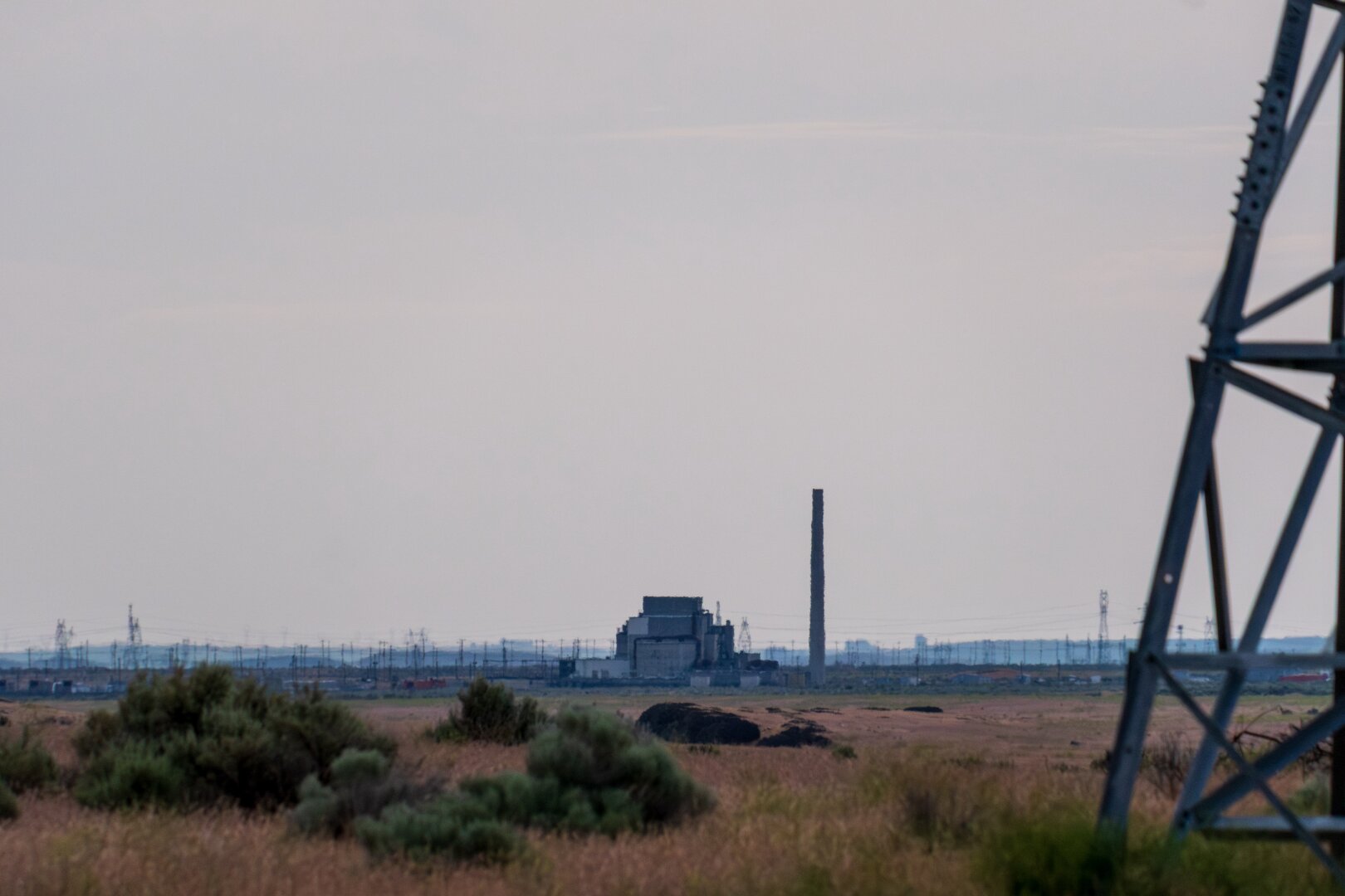 Amidst gray skies, a boxy structure sits in the distance on yellowish scrubland. [Fuji X-T5 / Tamron 18-300]