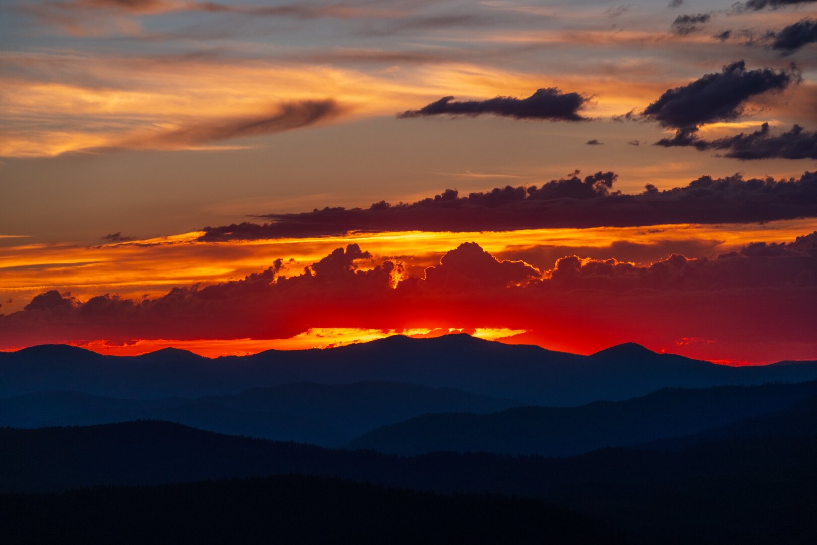 The sun sets in a cloudy sky, turning mountains purple. [Fuji X-T5 / Tamron 18-300]