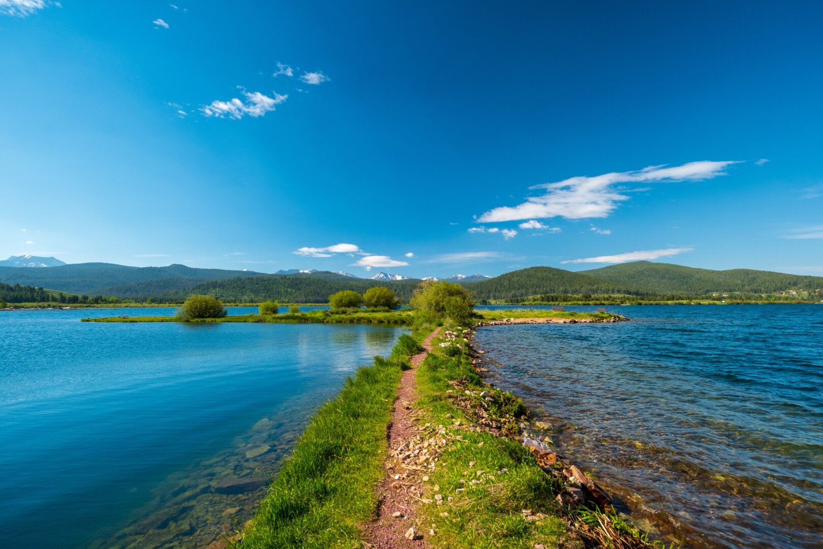 A little spit of grassy land heads into the water, with hills and mountains behind. [Fuji X-T5 / Fuji 10-24]