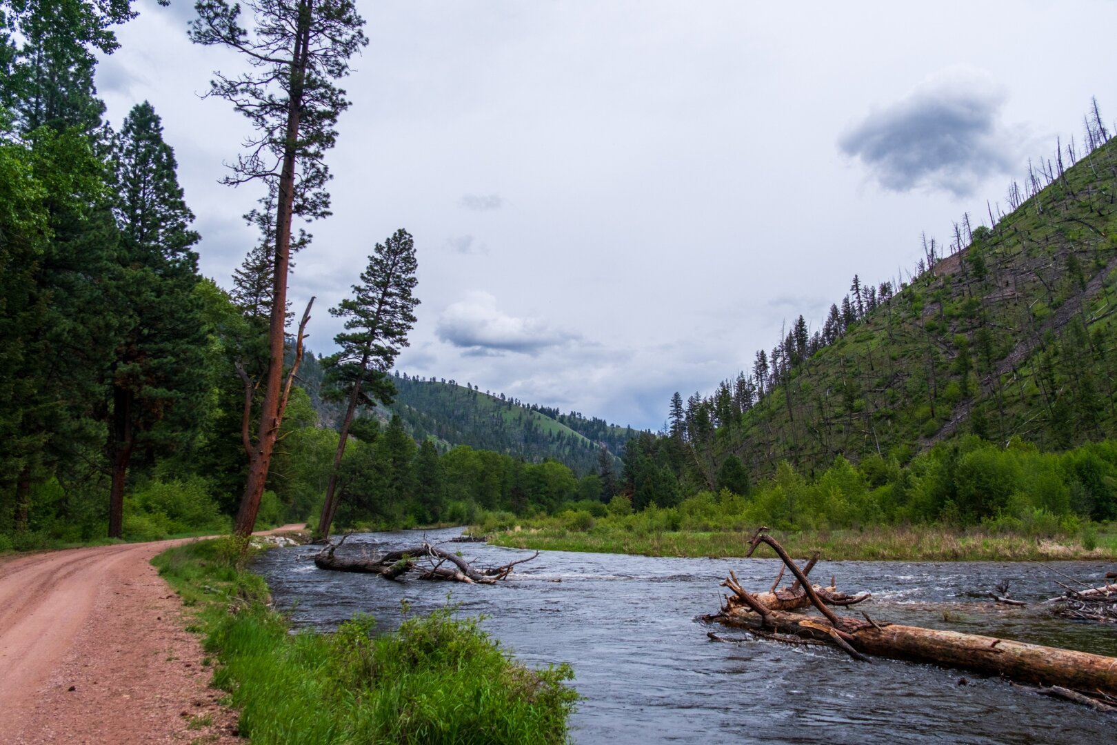 A river runs by a dirt road under cloudy skies. [Fuji X-T5 / Sigma 17-40 1.8]