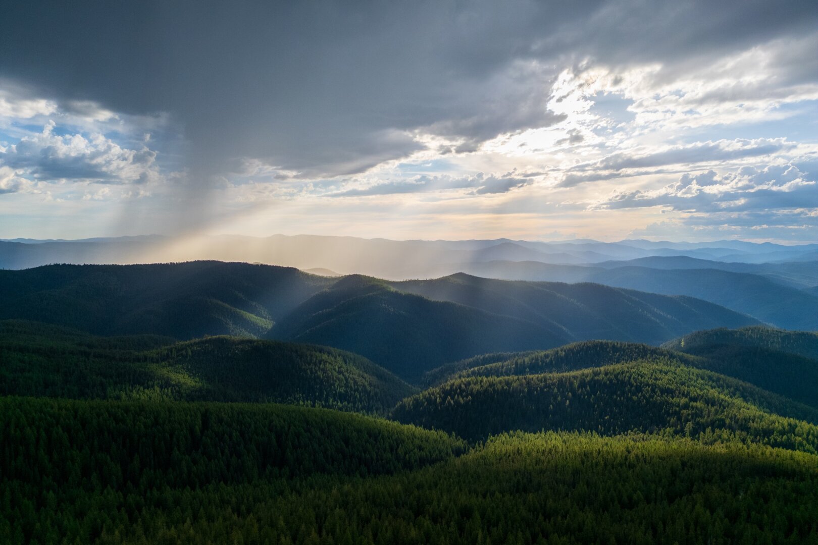 Sunrays shine through clouds onto hills. [DJI Mini 3 Pro]